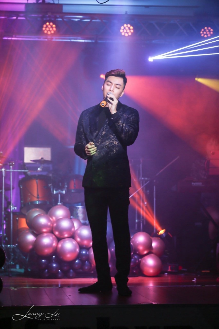 Đinh Công Phụng singing into a microphone under colorful stage lights