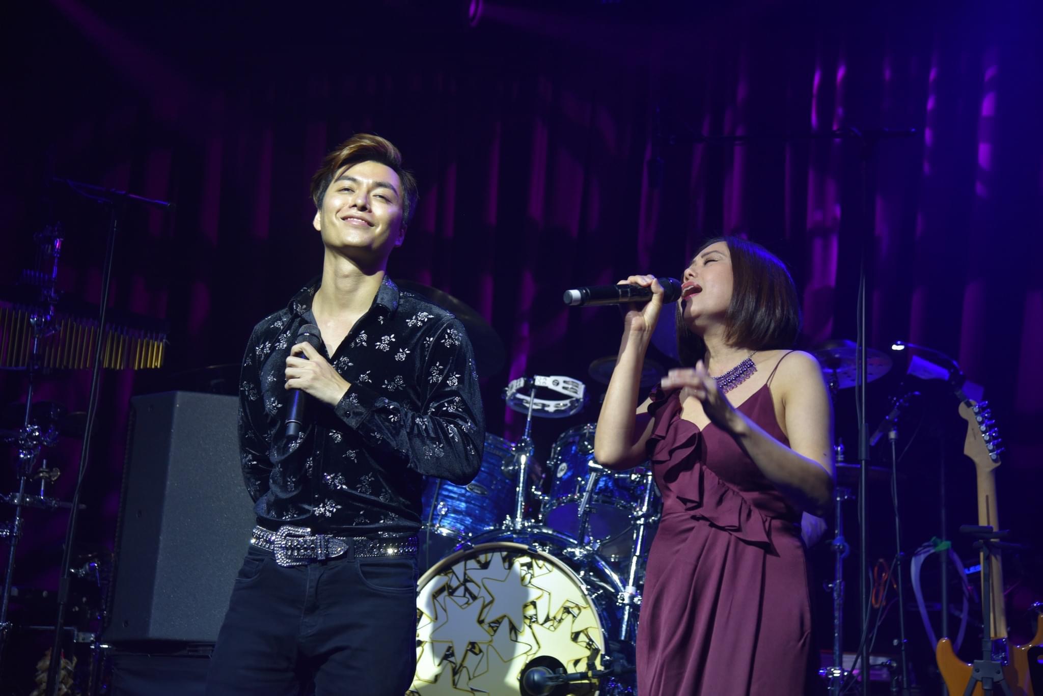 Two singers performing under violet stage lights